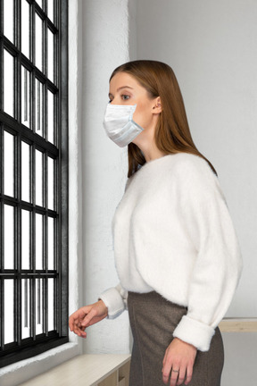 A woman wearing a face mask standing next to a window