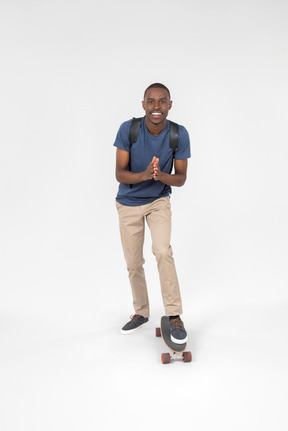 Black male tourist standing with one leg on skateboard and holding his hands folded