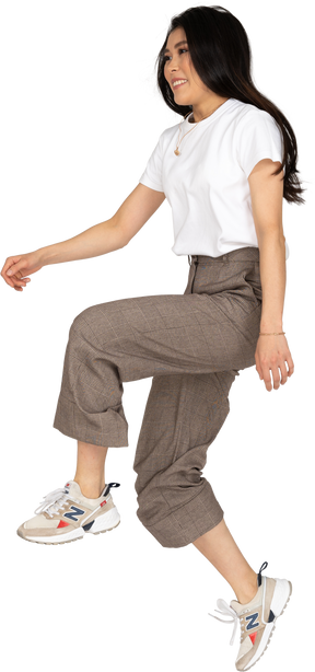 Vista lateral de una señorita saltando en calzones y camiseta levantando su pierna
