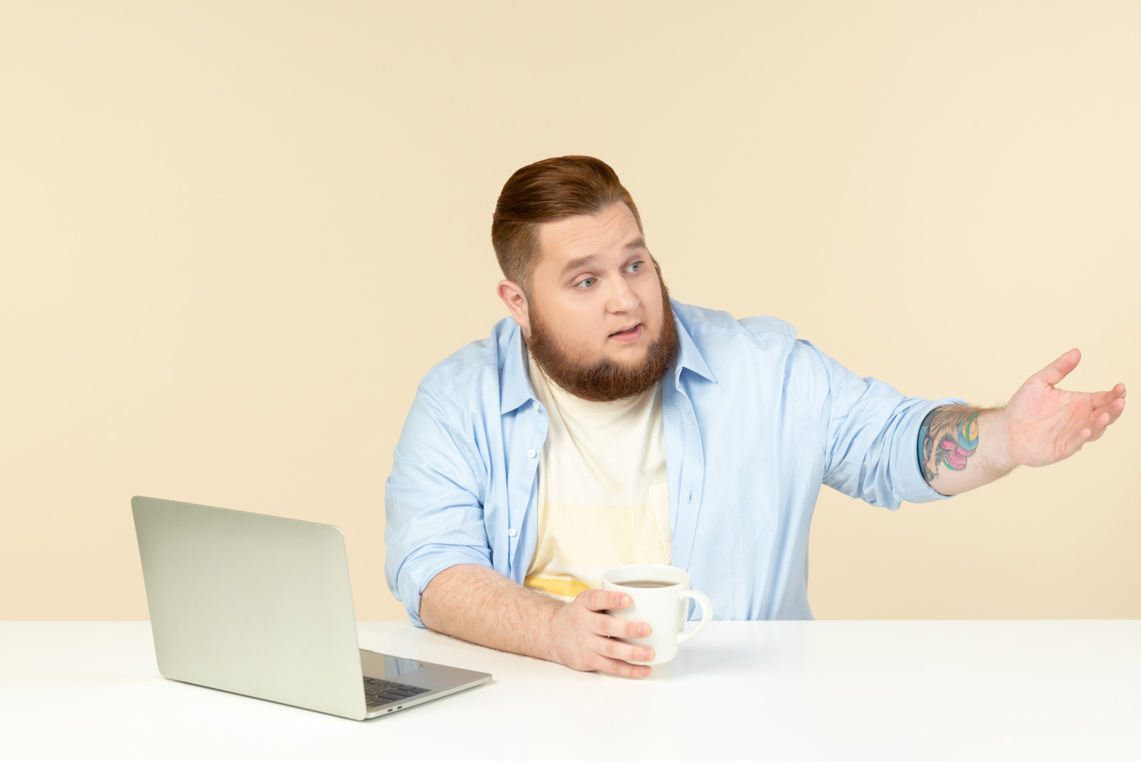 Young overweight man sitting in front of laptop and having tea