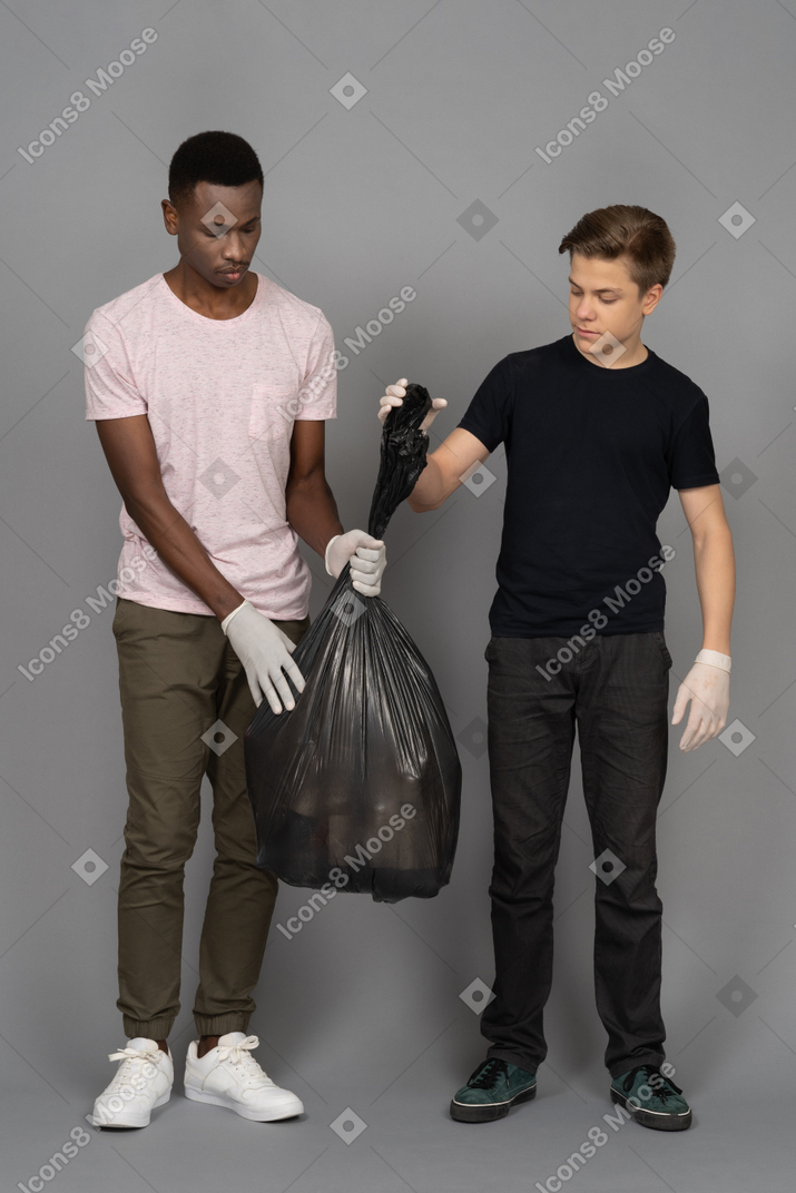 Two young men lifting a black trash bag