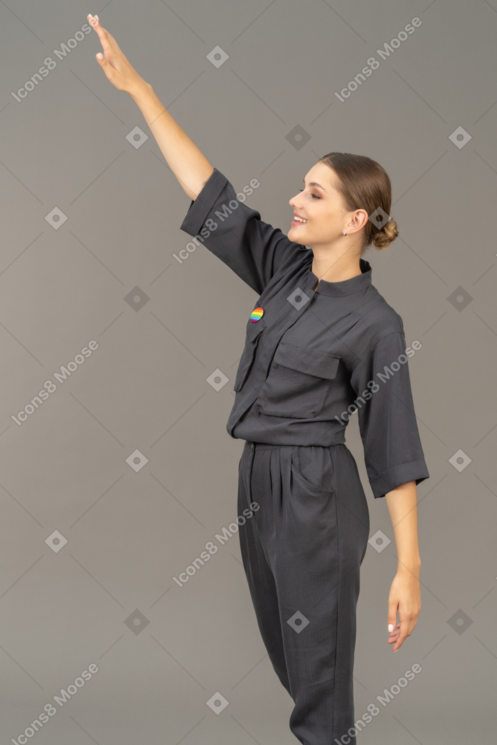 Side view of a cheerful young woman in a jumpsuit raising hand