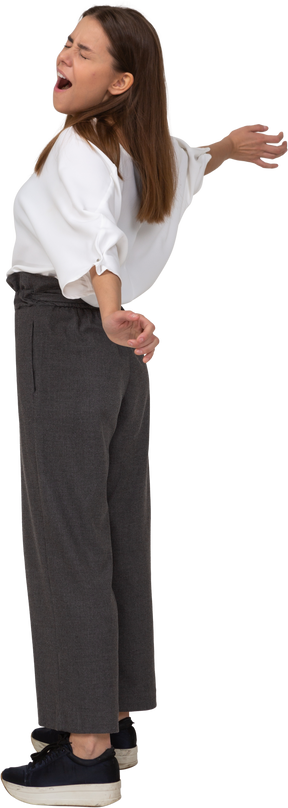Side view of a yawning young lady in office clothing outspreading her arms