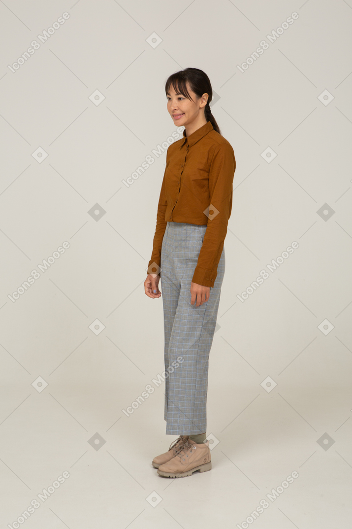 四分之三的视图是一位身着马裤和衬衫的微笑年轻亚洲女性站着不动