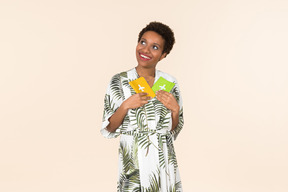 Black short-haired woman in a white and green dress, standing with two passports in her hands