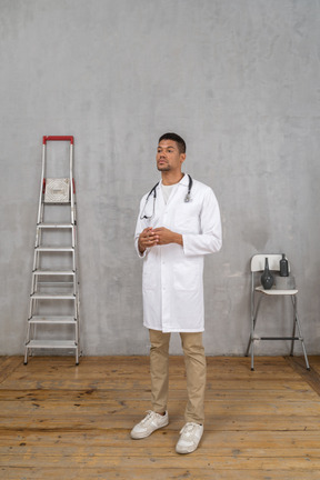 Vista de três quartos de um jovem médico em uma sala com escada e cadeira de mãos dadas