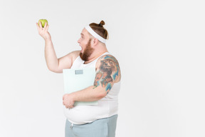 Excited young man holding scales and looking at green apple