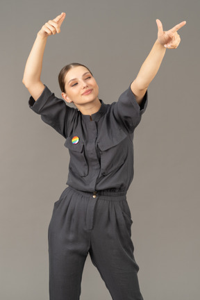 Vista frontal de una mujer joven en un mono con pin lgbt levantando las manos