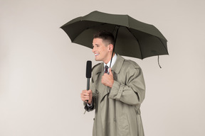Smiling male reporter holding microphone and standing under the umbrella