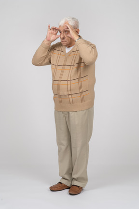 指を通して見ているカジュアルな服装の老人の正面図