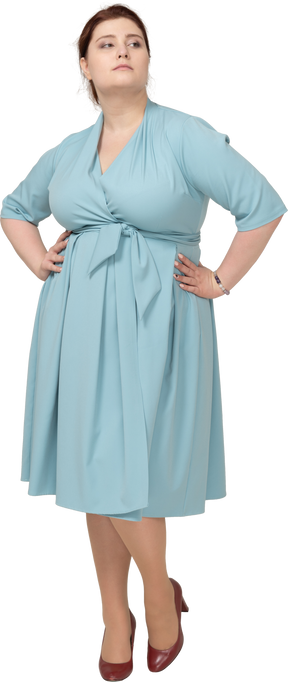 Vista frontal de uma mulher de vestido azul posando com as mãos na cintura