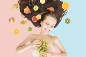 A young woman covered with fruits laying and holding grapes