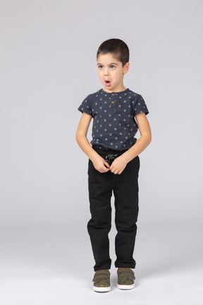 Vista frontal de um garoto impressionado em roupas casuais em pé e com a boca aberta