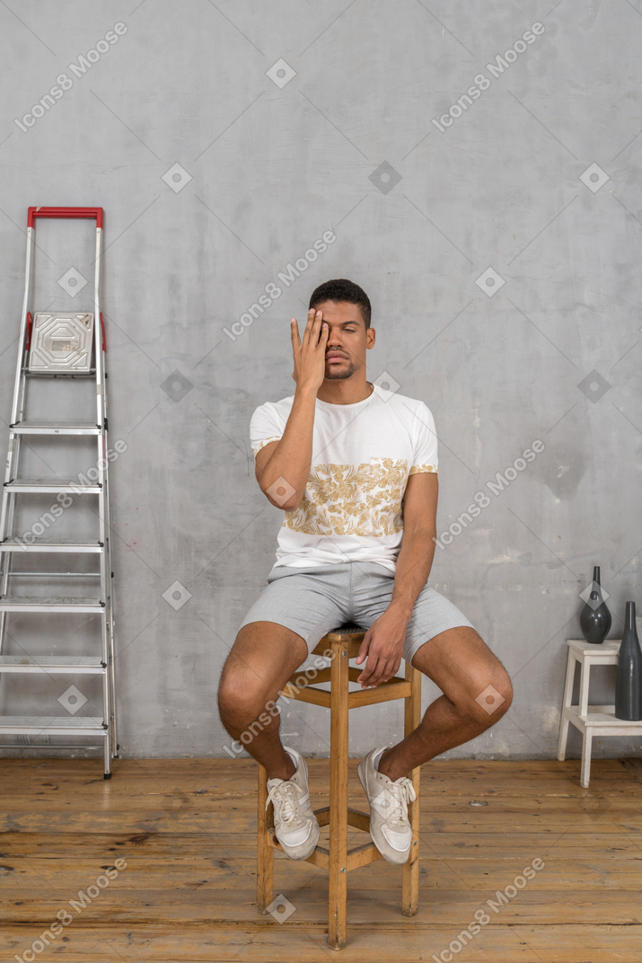 Young man sitting on chair and rubbing his eye