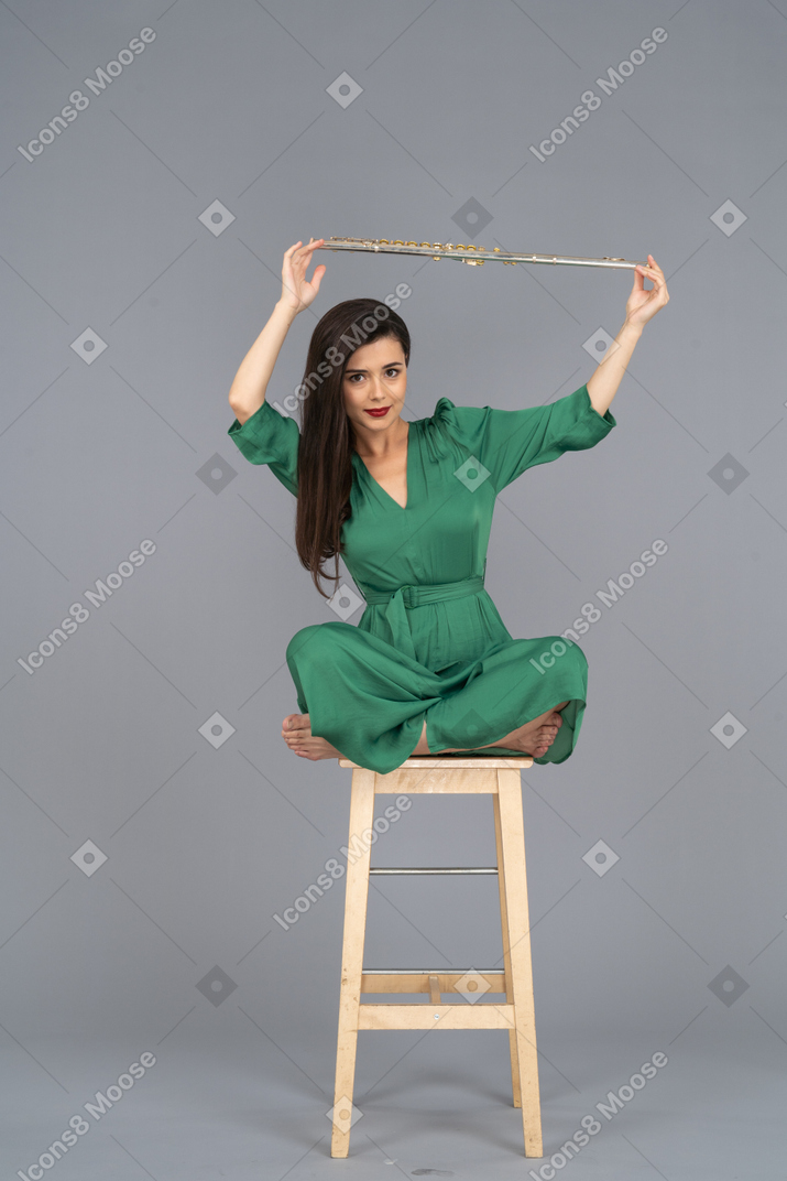 Full-length of a young lady holding her clarinet over head while sitting on a wooden chair