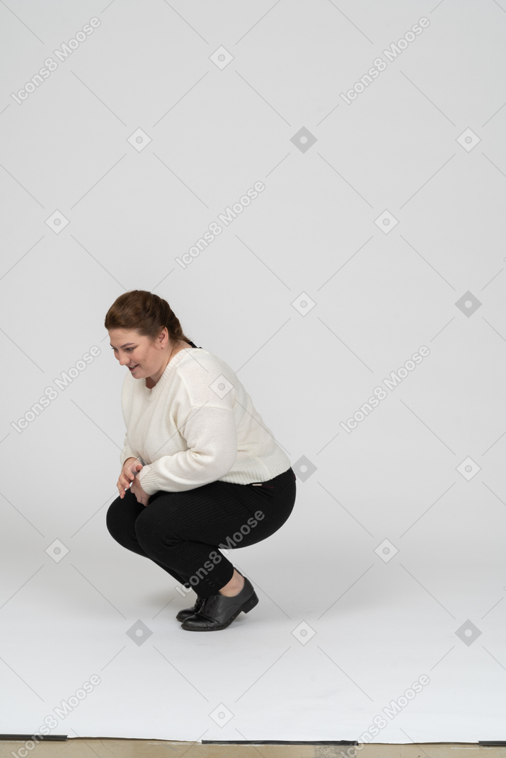 Vista lateral de una mujer regordeta en suéter blanco en cuclillas