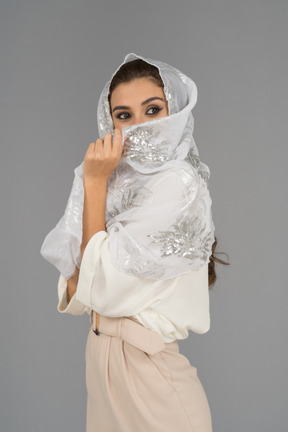 Fröhliche junge arabische frau, die gesicht mit weißem schal mit silberner stickerei bedeckt