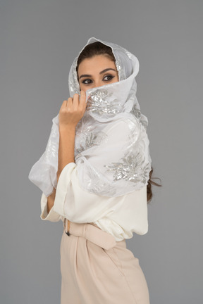 Cheerful young arab woman covering face with white shawl with silver embroidery