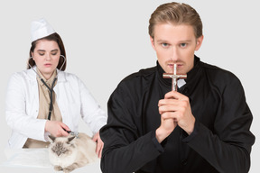 A vet examining a cat and a priest with a cross