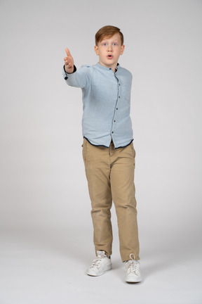 Vista frontal de um menino impressionado, apontando para a câmera com a mão