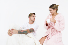 Pareja sentada en la cama y tomando un café