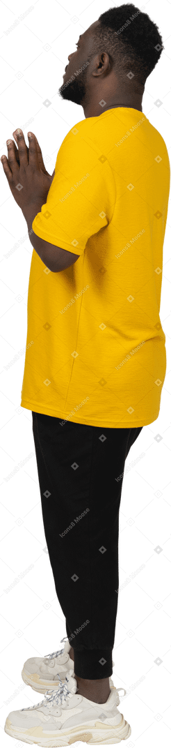 Вид сбоку на молодого темнокожего мужчину в желтой футболке, держащего руки вместе