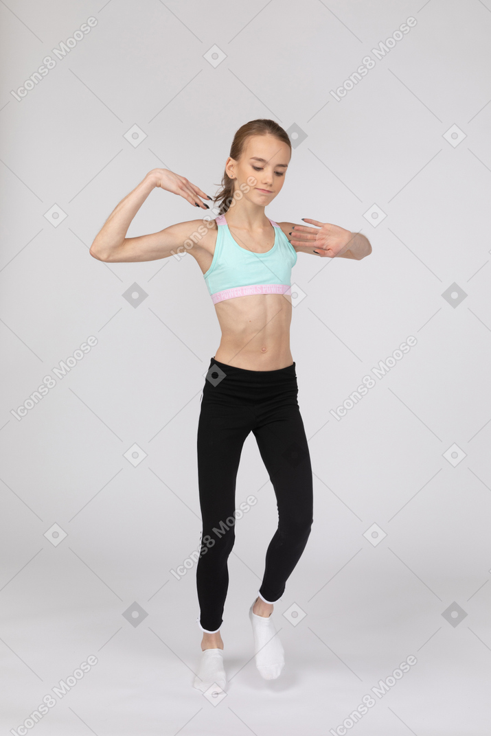 Vista de tres cuartos de una jovencita en ropa deportiva levantando ambas manos mientras baila