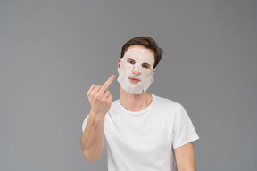 中指を示す顔のマスクの若い男の正面図