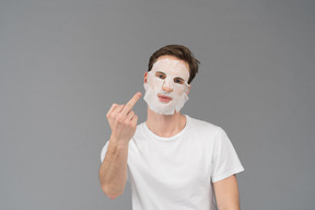 Front view of a young man in facial mask showing middle fingers