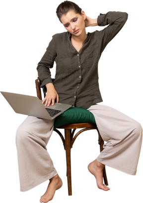 ノートパソコンで椅子に座って家の服を着て疲れた若い女性の正面図