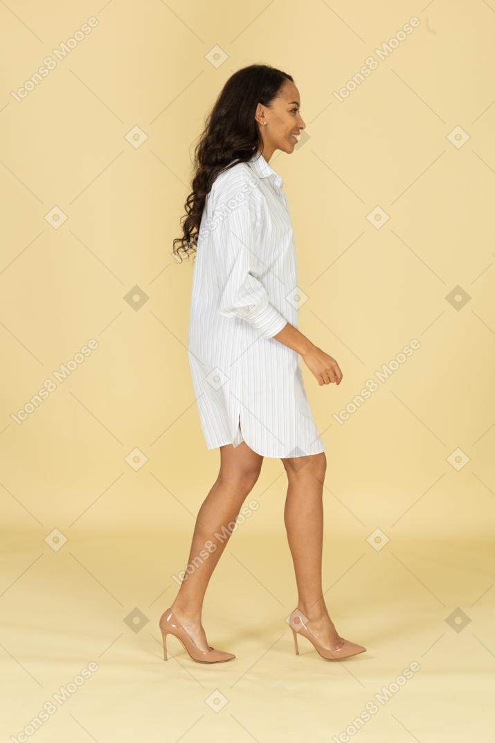 Side view of a smiling walking dark-skinned young female in white dress