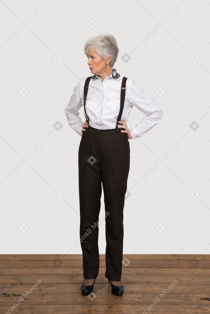 Front view of a displeased old lady in office clothing putting hands on hips
