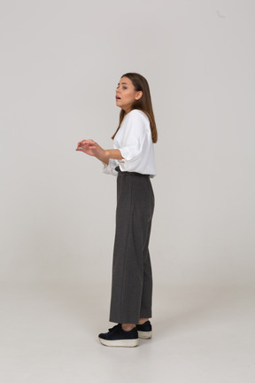 Side view of a shocked young lady in office clothing raising hands
