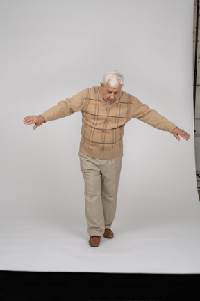 腕を伸ばして前に歩くカジュアルな服装の老人の正面図