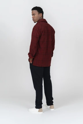 Three-quarter back view of man standing with hands in pockets