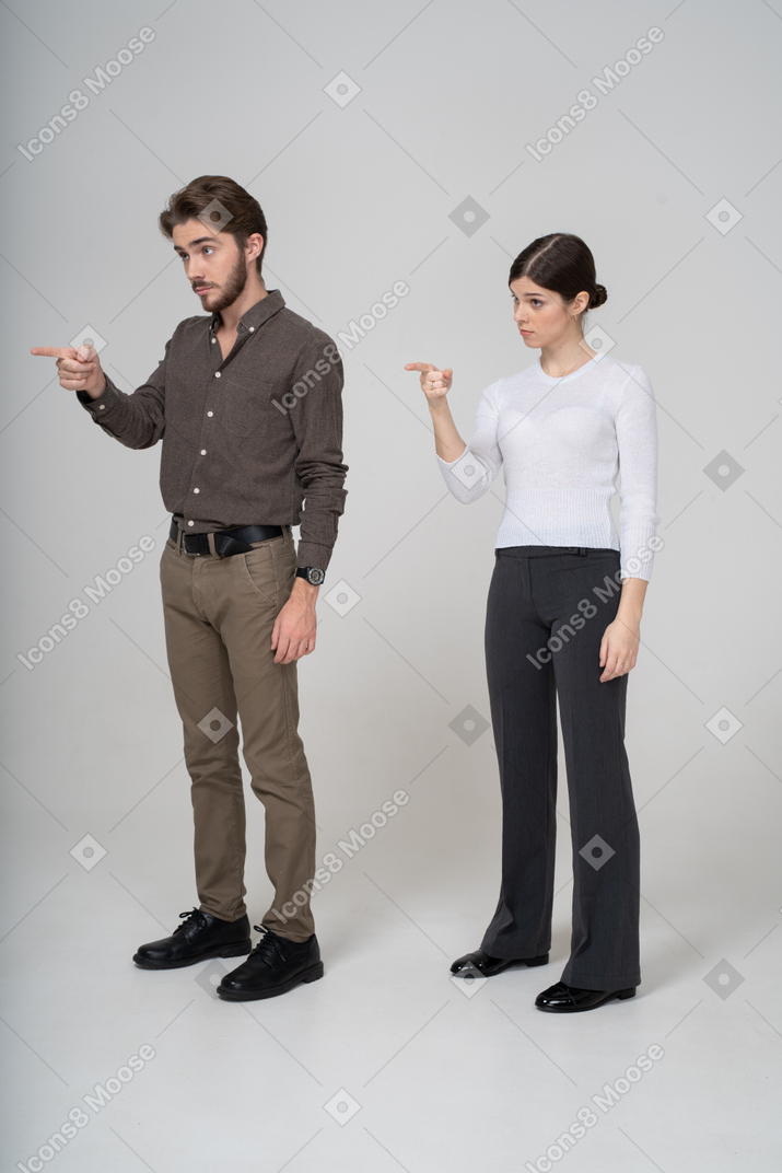Three-quarter view of a young couple in office clothing pointing finger forward