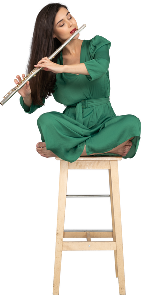 In voller länge eine junge dame, die klarinette spielt und mit gekreuzten beinen auf einem holzstuhl sitzt
