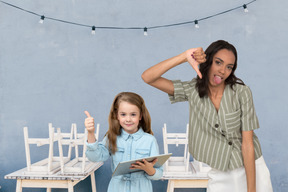 Kid fille montrant les pouces vers le haut tandis que la jeune femme montrant les pouces vers le bas