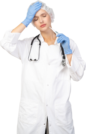 Vue de face d'une jeune femme médecin avec stéthoscope tenant un thermomètre et touchant la tête
