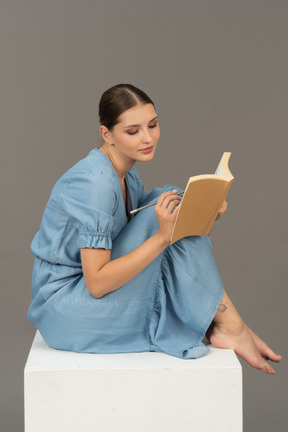Vista lateral de una joven sentada en un cubo y escribiendo en un cuaderno