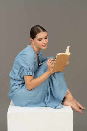 Side view of young woman sitting on a cube and writing in notebook