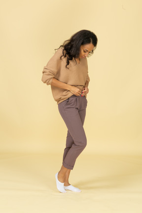 Vista de tres cuartos de una mujer joven de piel oscura subiendo la cremallera de sus pantalones