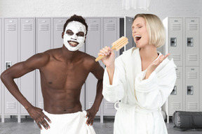 Woman singing into hairbrush next to man doing facial mask