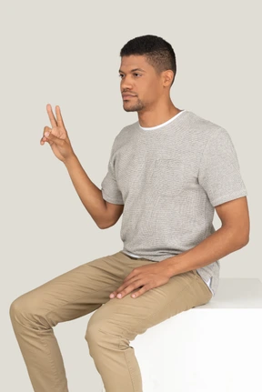 A three-quarter side view of a beautiful young man sitting on the white chair and looking to the left