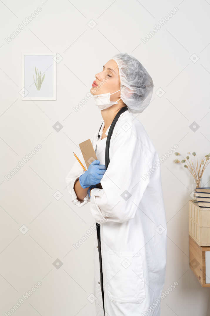 Vista lateral de uma jovem médica sonolenta segurando um lápis e um tablet