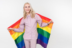 Junge blonde person in pastell-pjs und eine regenbogenfahne in ihren händen, stehend gegen den einfachen weißen hintergrund