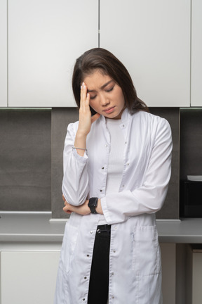 Vista frontale del medico femminile stanco guardando in basso e toccando la fronte