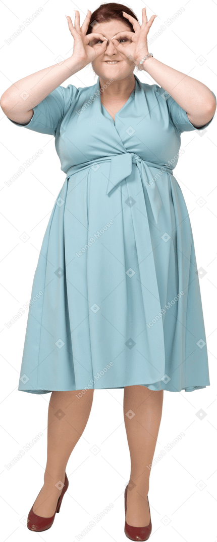 Vista frontal de una mujer en vestido azul mirando a través de binoculares imaginarios