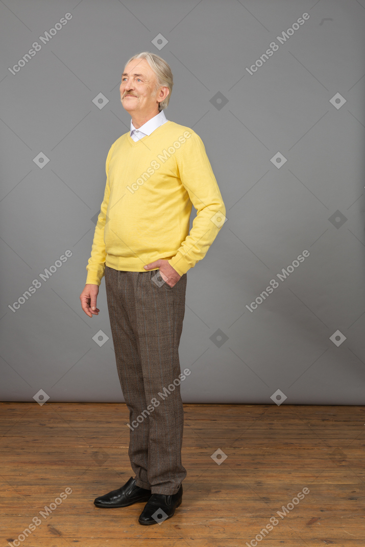 一件黄色套头衫的高兴老人的四分之三视图，将手放在口袋里，放在一边