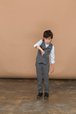 Vista frontal de um menino bonito de terno cinza, mostrando o polegar para baixo